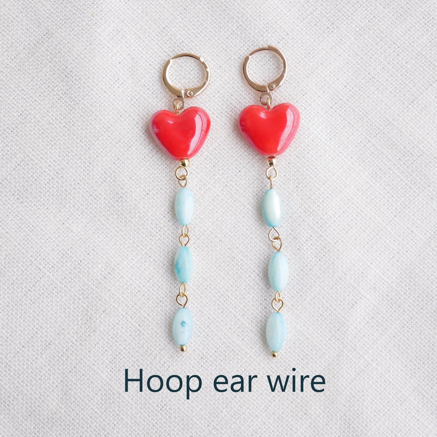 Long dangle earrings with red porcelain hearts and turquoise shell beads, on a white cloth.