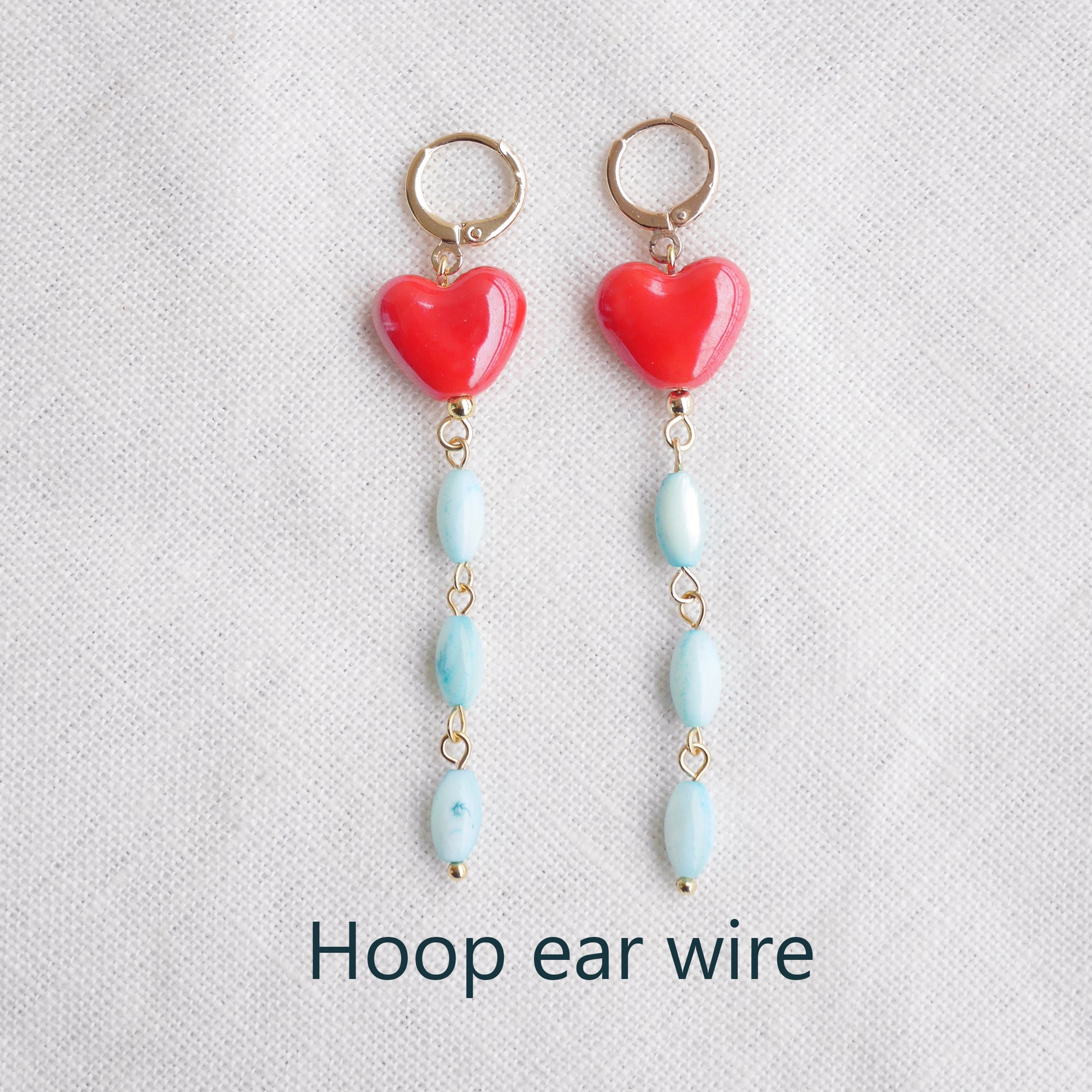 Long dangle earrings with red porcelain hearts and turquoise shell beads, on a white cloth.