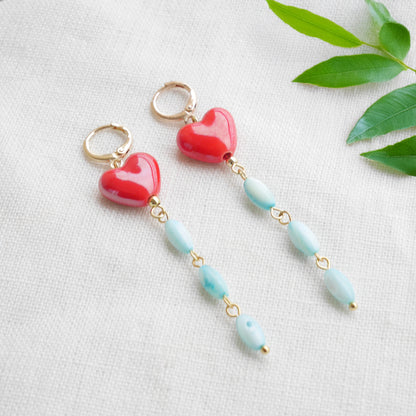 Long dangle earrings with red porcelain hearts and turquoise shell beads, on a white cloth.