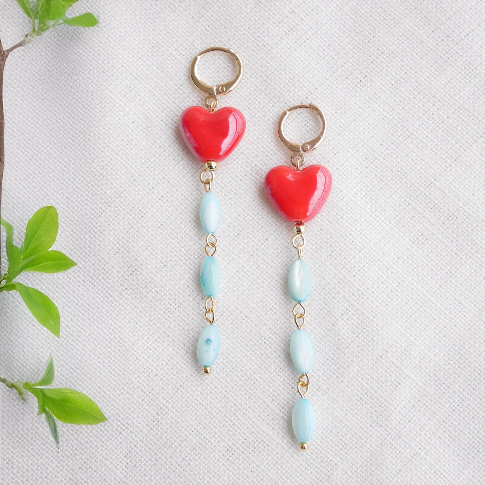 Long dangle earrings with red porcelain hearts and turquoise shell beads, on a white cloth.