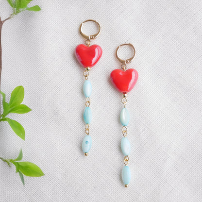Long dangle earrings with red porcelain hearts and turquoise shell beads, on a white cloth.