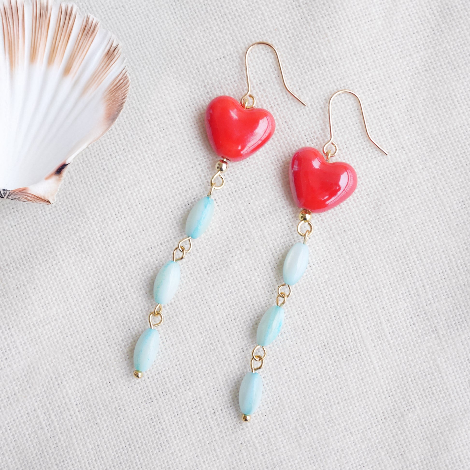Long dangle earrings with red porcelain hearts and turquoise shell beads, on a white cloth.