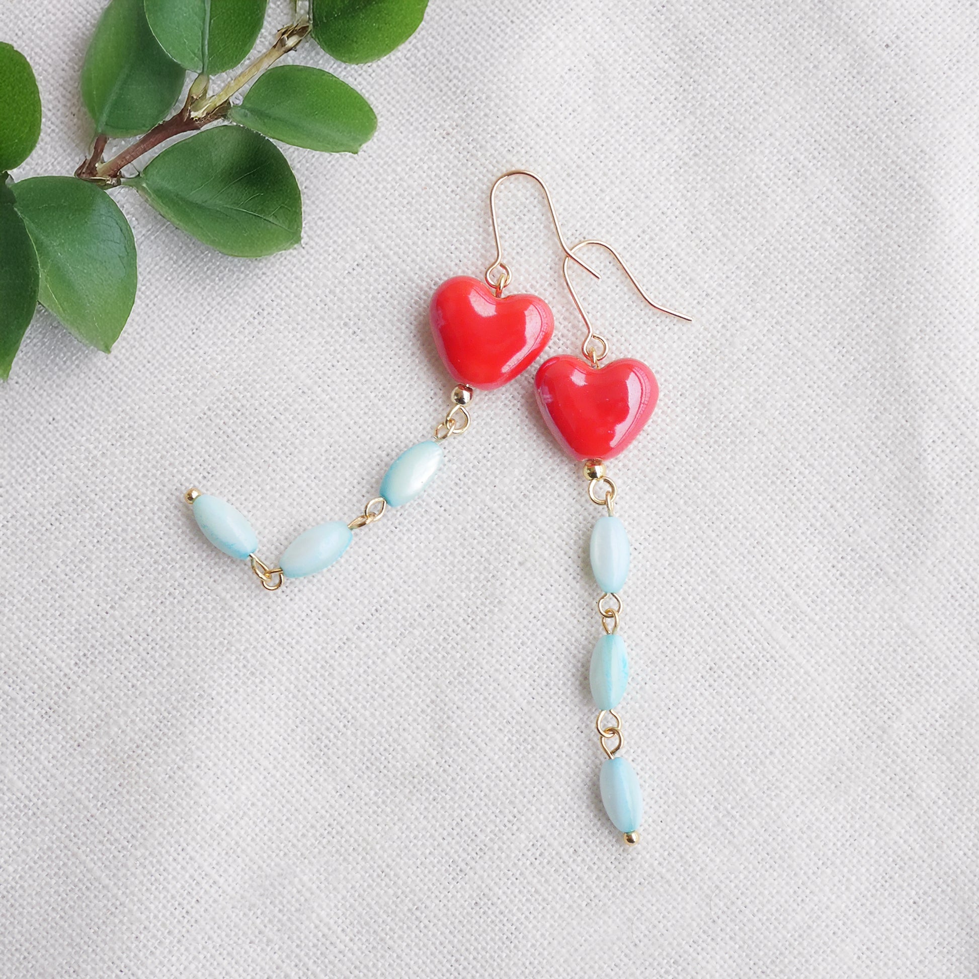 Long dangle earrings with red porcelain hearts and turquoise shell beads, on a white cloth.