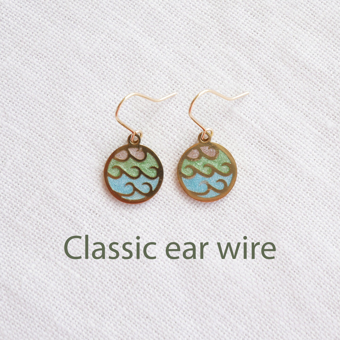 Gold wave charm disc earrings on a white cloth.