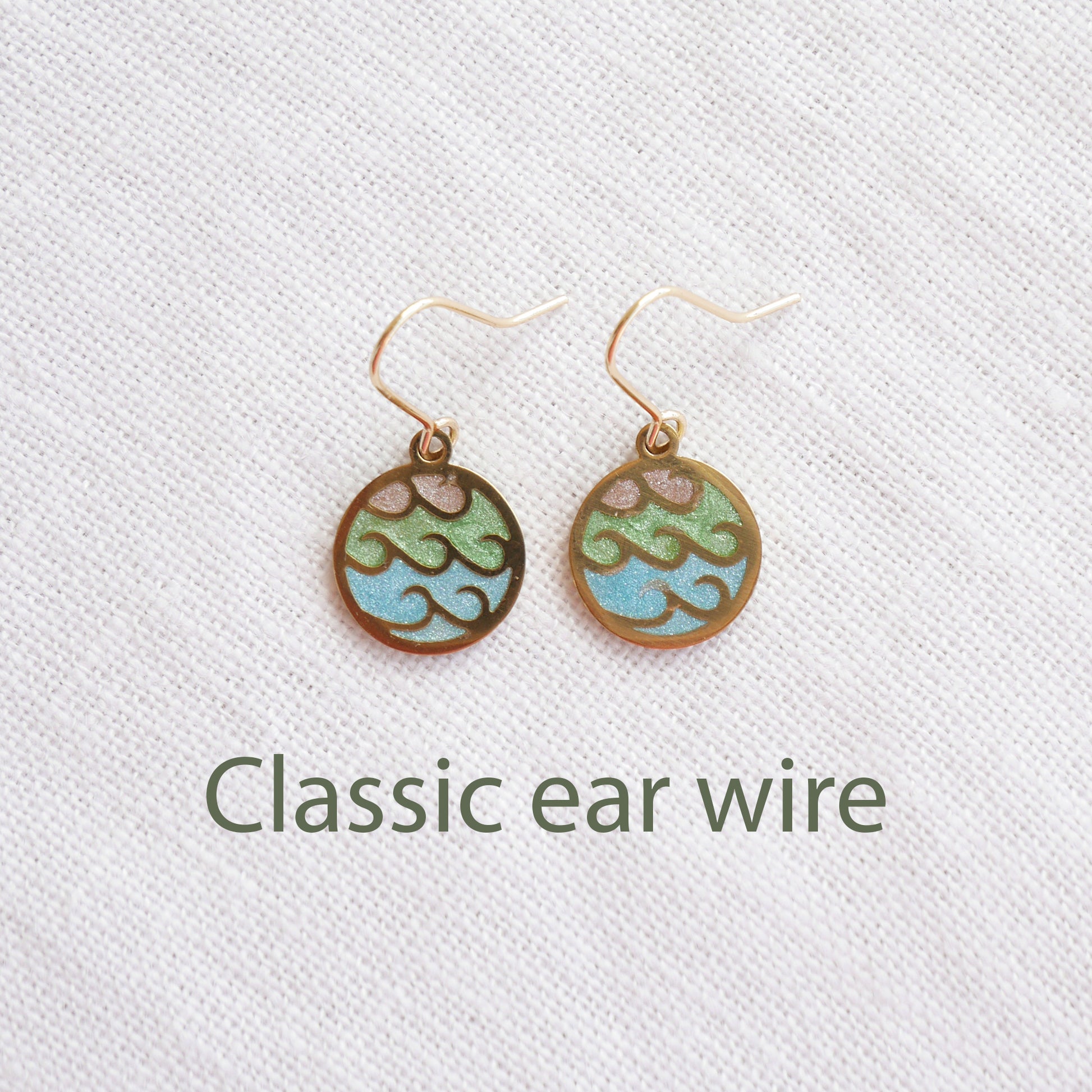 Gold wave charm disc earrings on a white cloth.