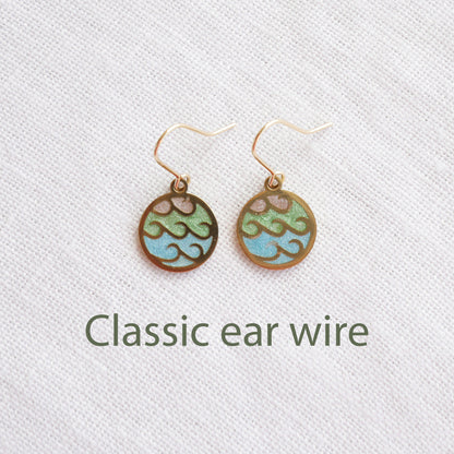 Gold wave charm disc earrings on a white cloth.