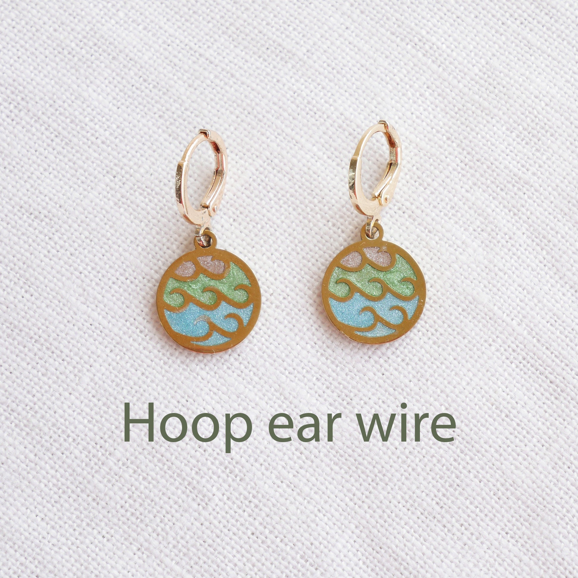 Gold wave charm disc earrings on a white cloth.