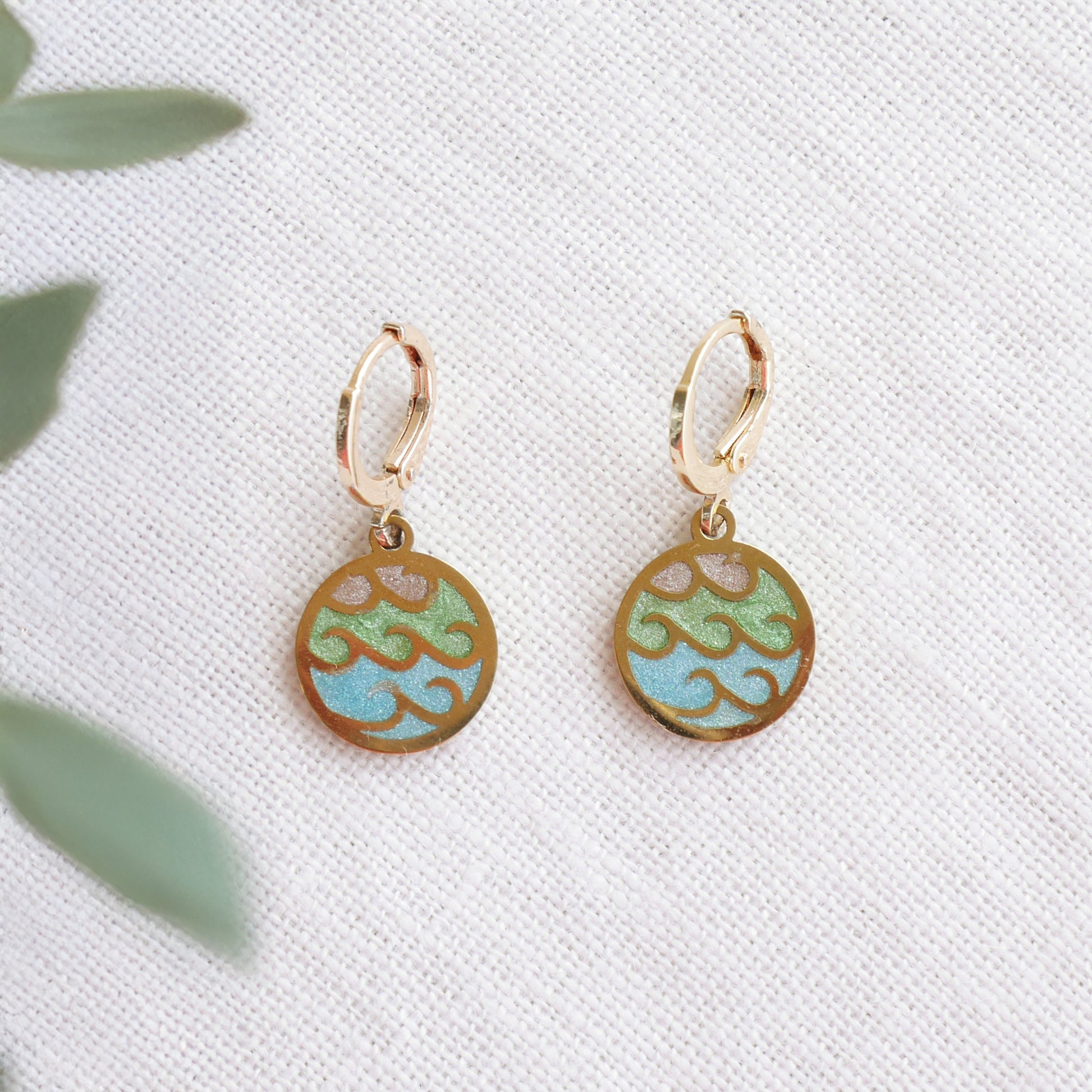 Gold wave charm disc earrings on a white cloth.