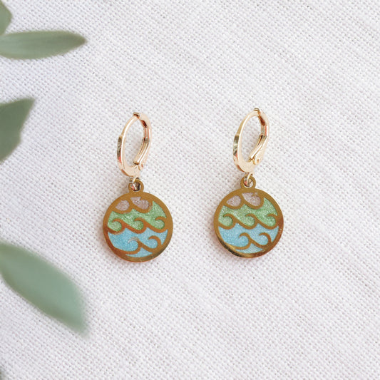 Gold wave charm disc earrings on a white cloth.
