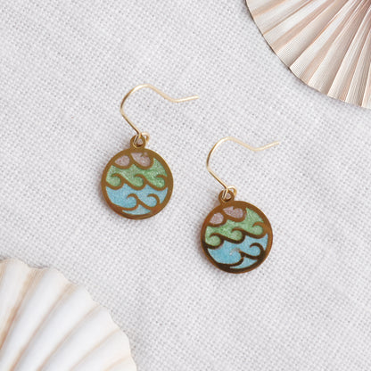 Gold wave charm disc earrings on a white cloth.