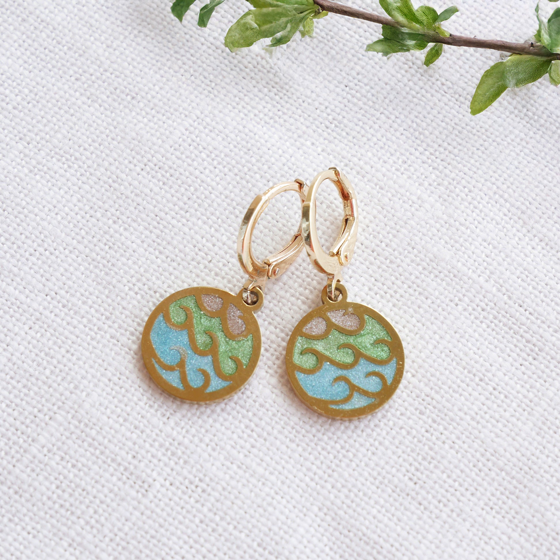 Gold wave charm disc earrings on a white cloth.