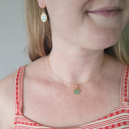 Woman wearing wave gold disc charm necklace and matching earrings.