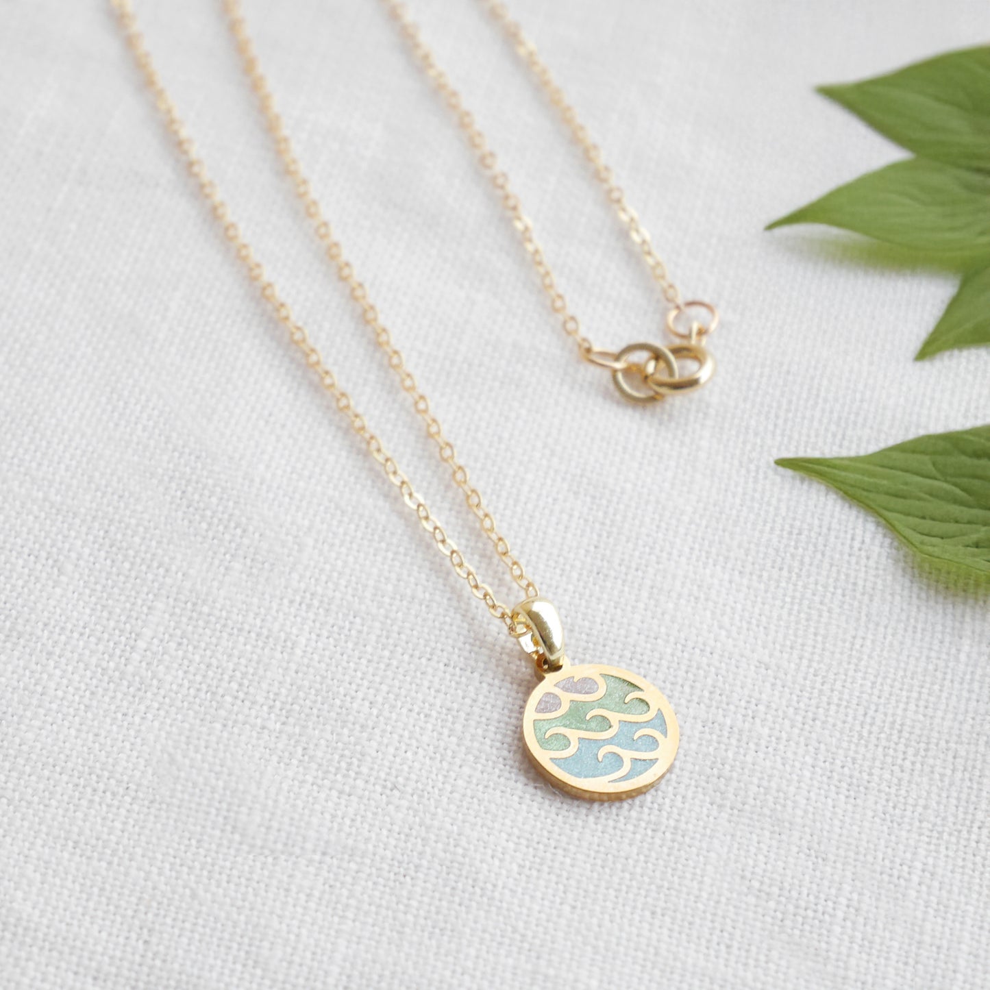 Wave gold disc charm necklace on a white cloth.
