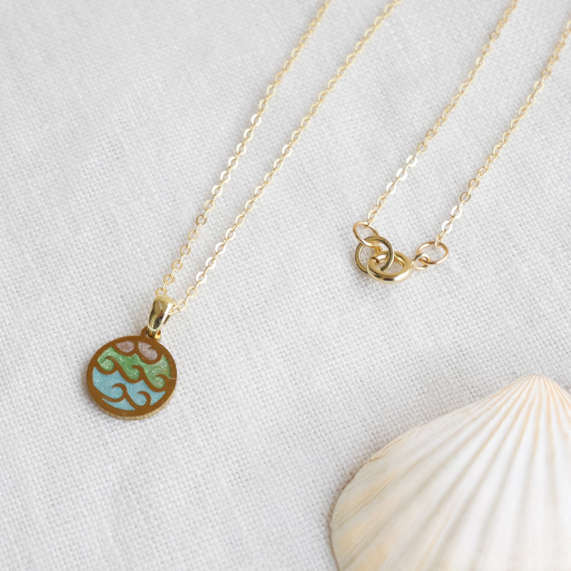 Wave gold disc charm necklace on a white cloth.