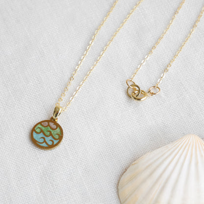 Wave gold disc charm necklace on a white cloth.