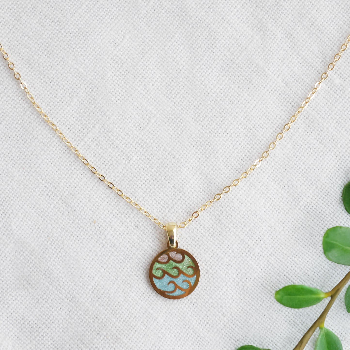 Wave gold disc charm necklace on a white cloth.