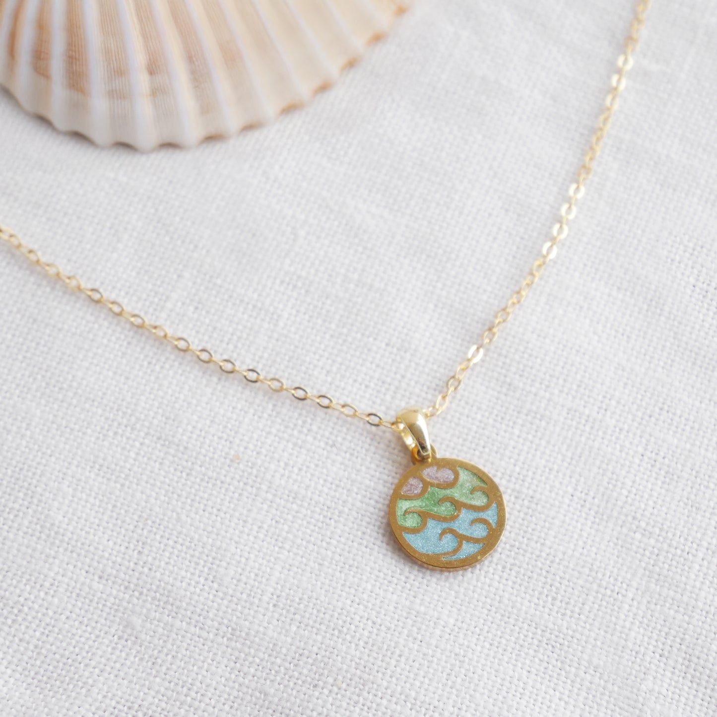 Wave gold disc charm necklace on a white cloth.