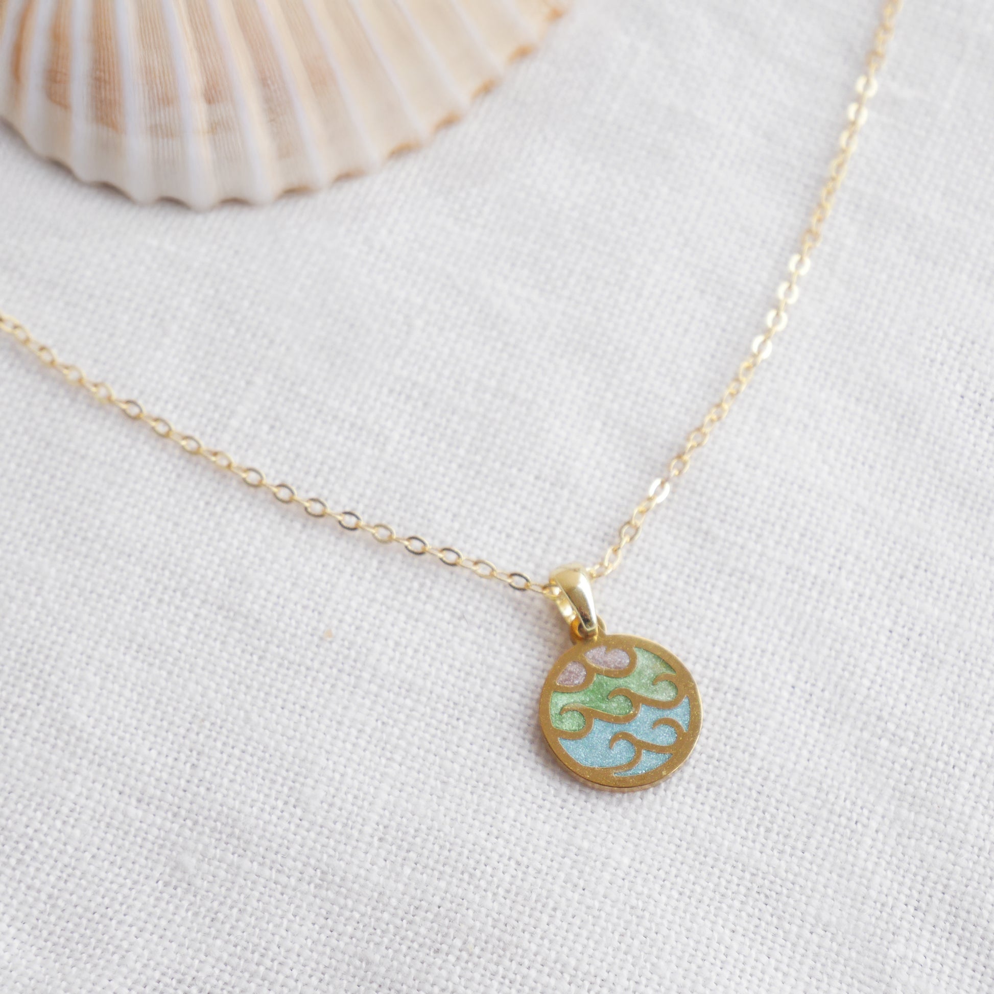 Wave gold disc charm necklace on a white cloth.