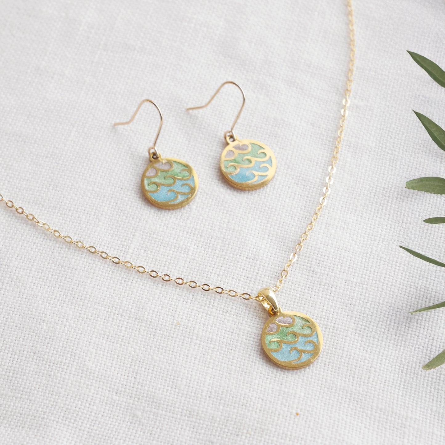 Wave gold disc charm necklace with a pair of earrings on a white cloth.