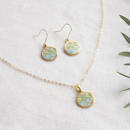 Wave gold disc charm necklace with a pair of earrings on a white cloth.