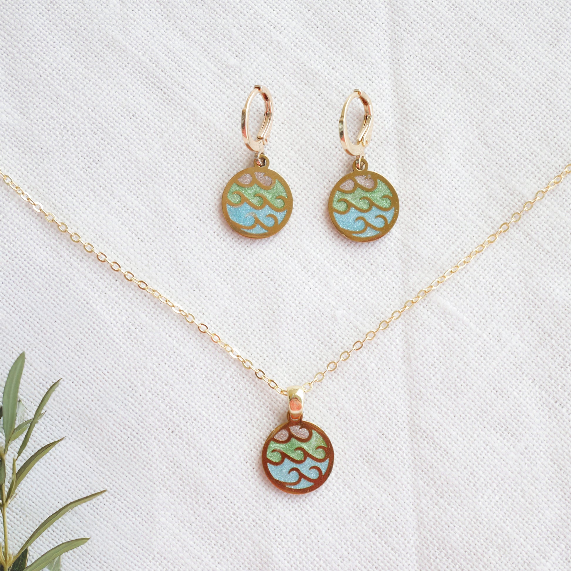 Wave gold disc charm necklace with a pair of earrings on a white cloth.