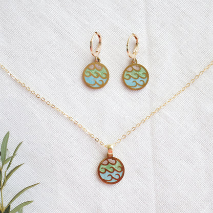 Wave gold disc charm necklace with a pair of earrings on a white cloth.