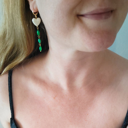Woman wearing heart-shaped earrings with white porcelain heart and green shell beads.