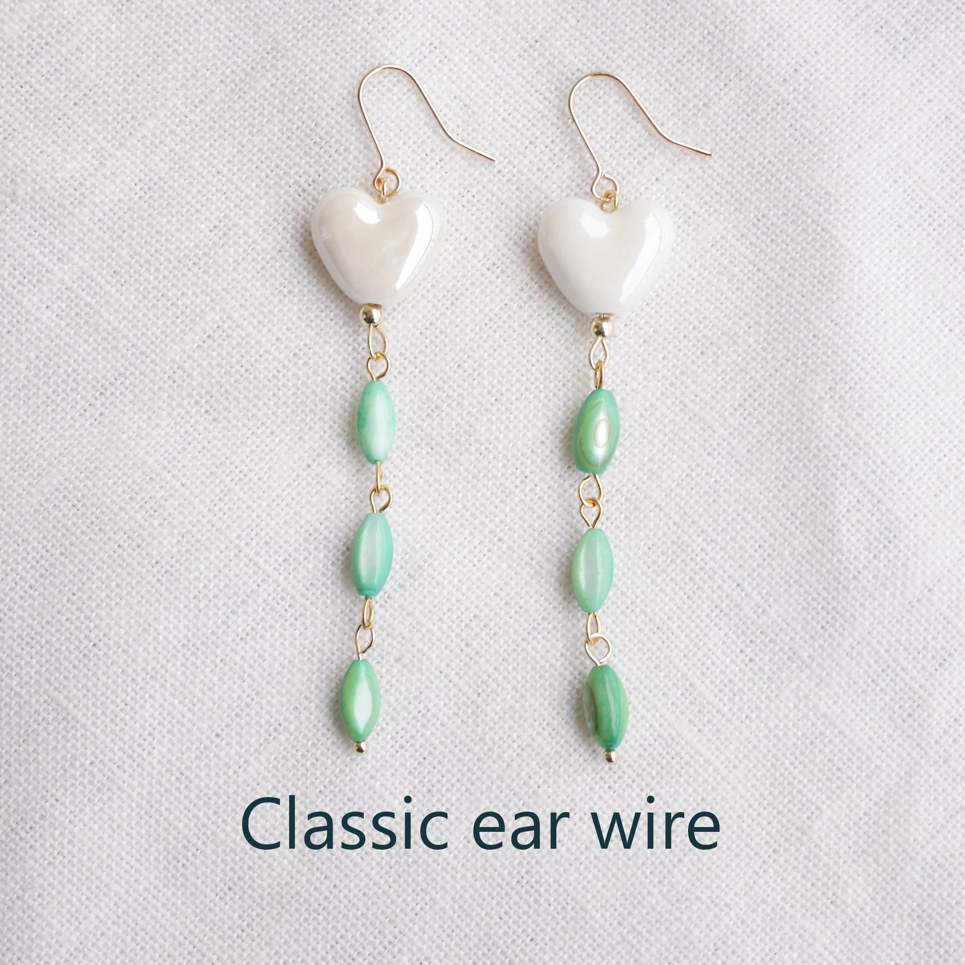 Pair of heart-shaped earrings with white porcelain heart and green shell beads on a light background.