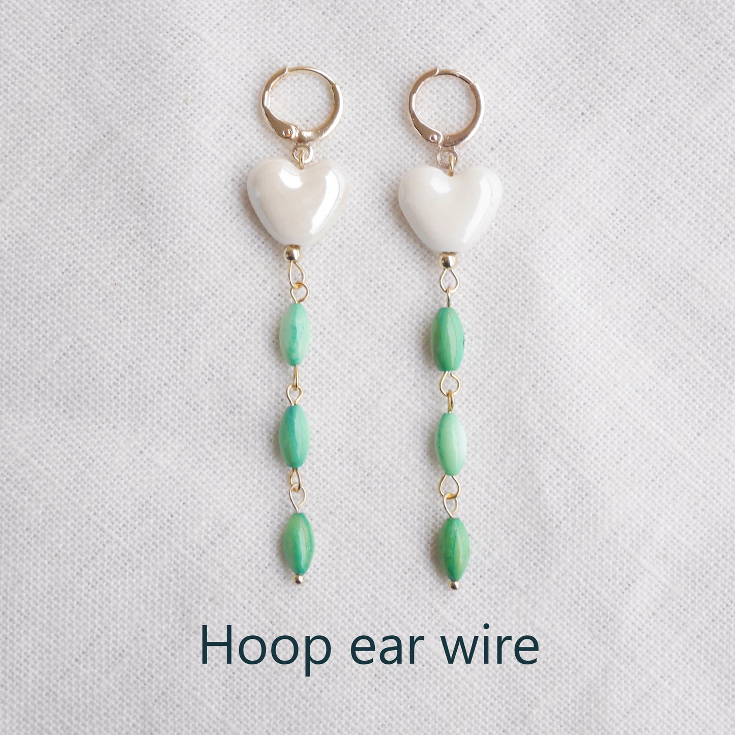 Pair of heart-shaped earrings with white porcelain heart and green shell beads on a light background.