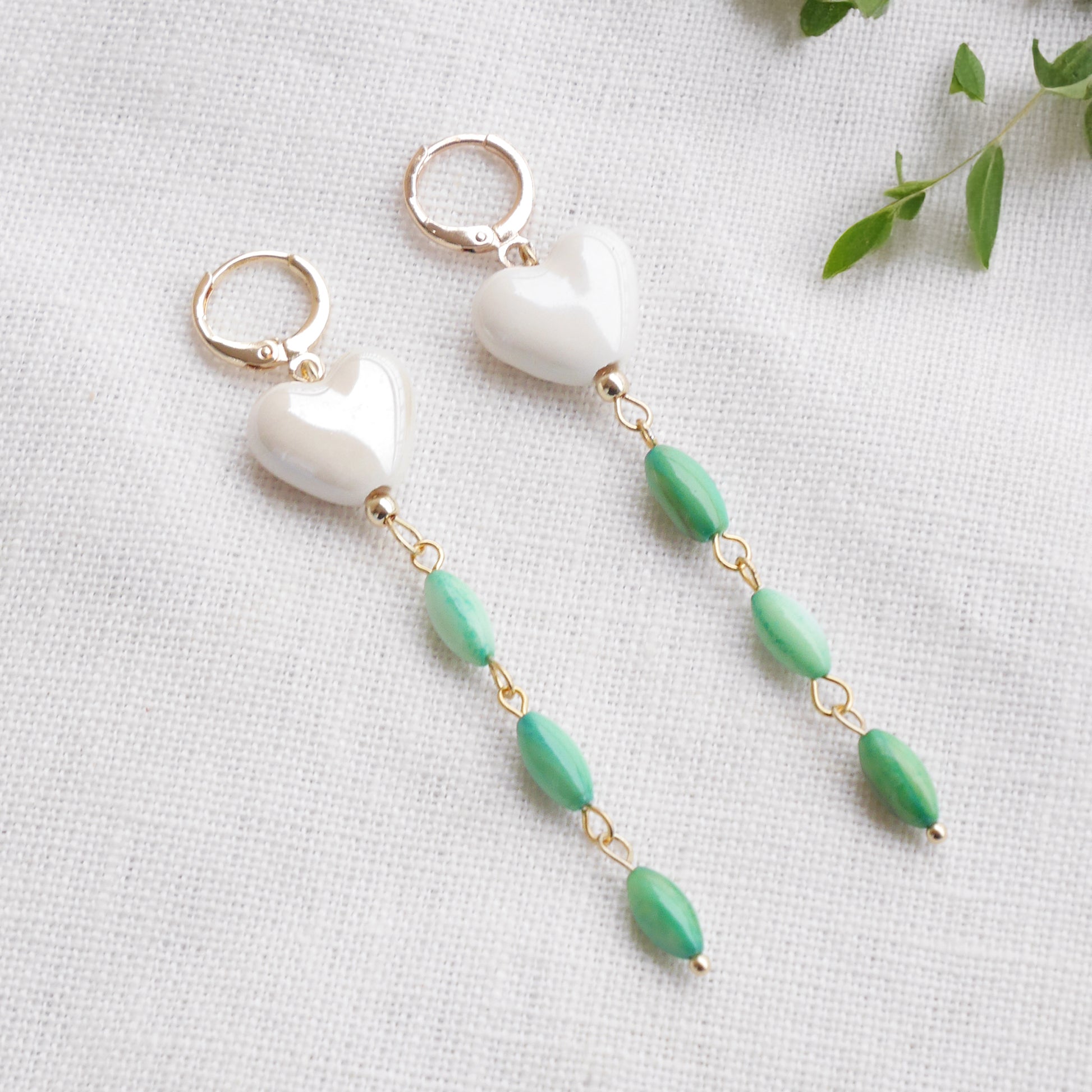 Pair of heart-shaped earrings with white porcelain heart and green shell beads on a light background.